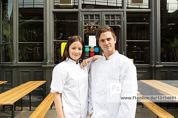 Couple in chef uniforms standing outside of work