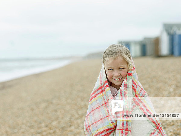 junges Mädchen kauert in Decke am Strand