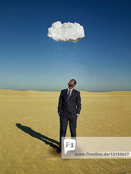 Geschäftsmann steht unter Regenwolke in der Wüste