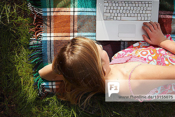 Frau auf Decke liegend mit Laptop