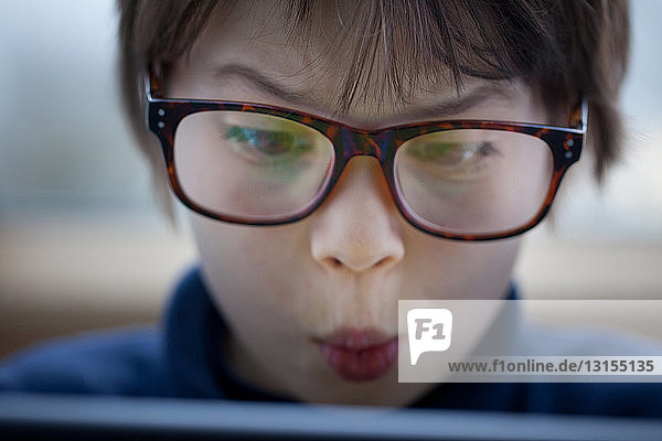 Nahaufnahme eines Jungen  der mit einem digitalen Tablet ein Gesicht zieht