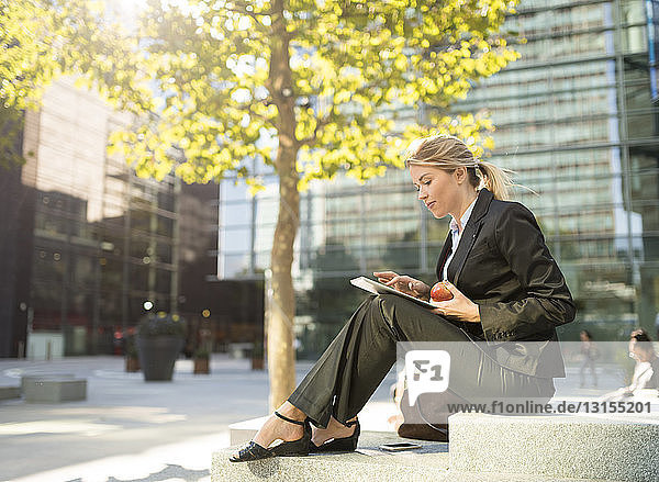 Junge Geschäftsfrau  die vor einem Büro in der Stadt sitzt und ein digitales Tablet benutzt