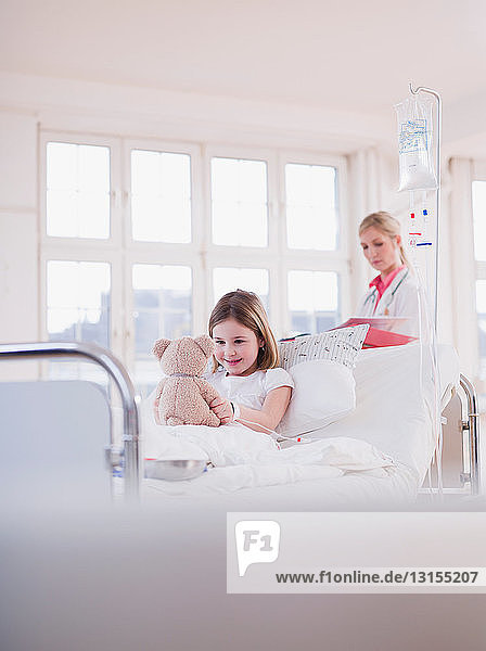 Sanitäterin und Mädchen im Bett mit Teddybär