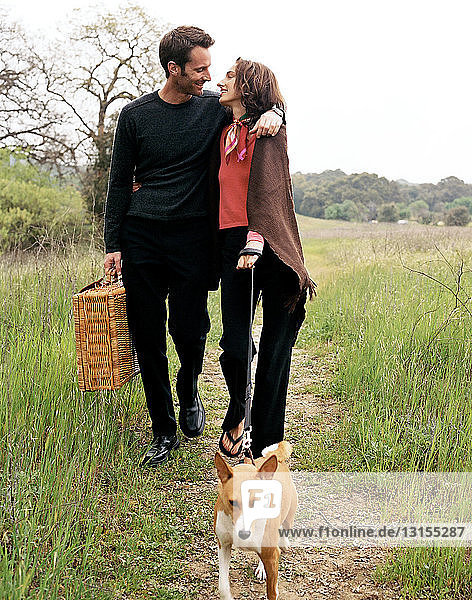 Ehepaar geht mit Hund in der Natur spazieren  mit Picknickkorb