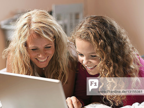 Junge Frau und Mutter schauen auf einen Laptop auf dem Bett