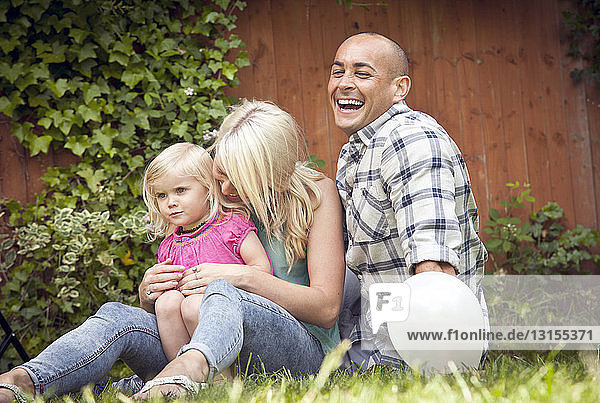 Glückliches Paar mit kleiner Tochter im Garten sitzend