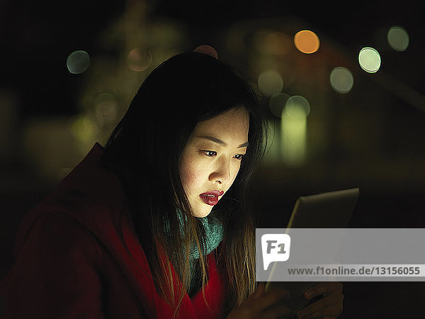 Junge Frau im Freien bei Nacht  Gesicht von digitalem Tablet beleuchtet