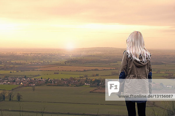 Junge Frau betrachtet den Sonnenaufgang über einer ländlichen Landschaft