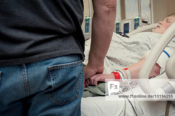 Mann hält die Hand einer Frau im Krankenhauszimmer
