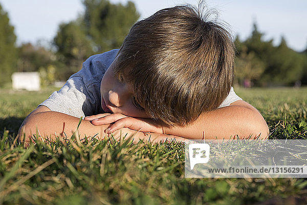 Mürrischer Junge mit gesenktem Kopf auf einer Parkwiese liegend