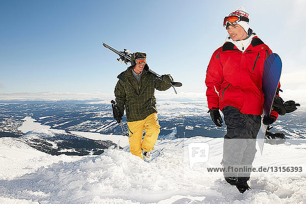 Snowboarder und Skifahrer  die ihre Ausrüstung zum Gipfel des Berges tragen