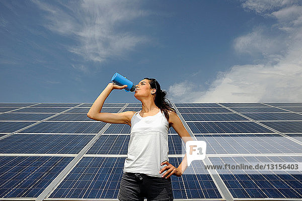 Frau trinkt vor einem Sonnenkollektor