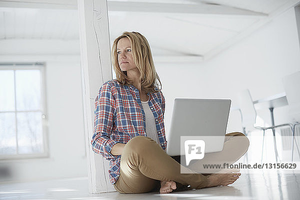 Porträt einer reifen Frau  die einen Laptop in einem leeren Büroraum benutzt