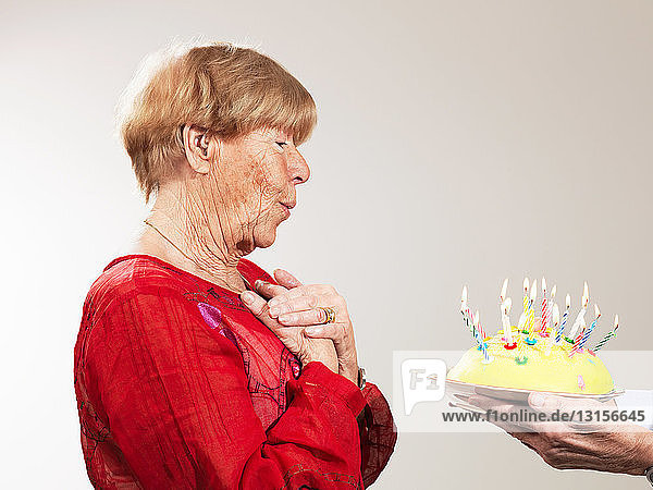 Senior woman receiving birthday cake against white background