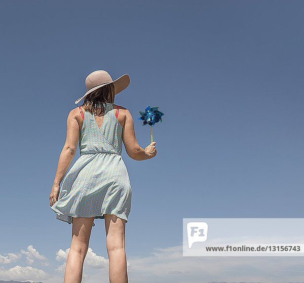 Rückansicht einer Frau mit Hut  die eine Papierwindmühle hält