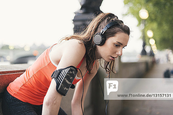 Exhausted female runner wearing headphones taking a break on riverside