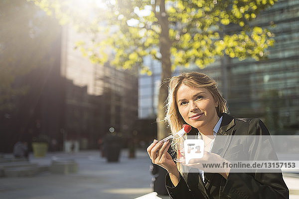 Porträt einer jungen Geschäftsfrau vor einem Büro in der Stadt  die Erdbeeren isst