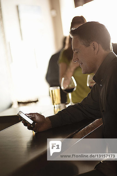 Geschäftsmann schaut in einer Weinstube auf sein Handy
