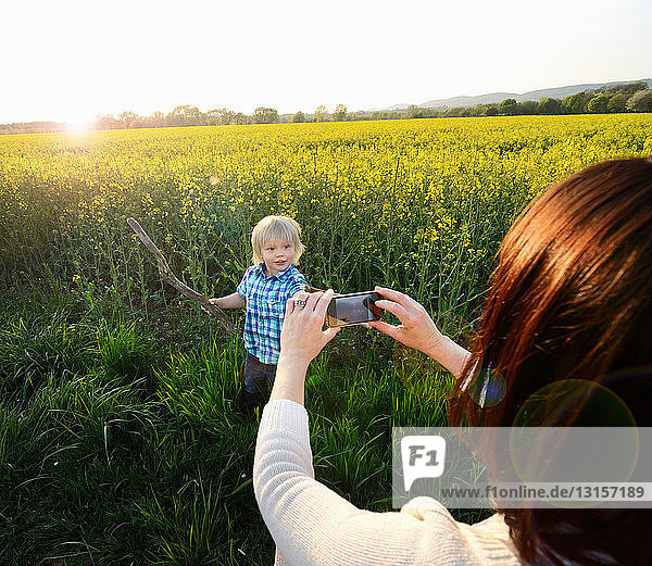 Mutter fotografiert Sohn mit Smartphone im Feld