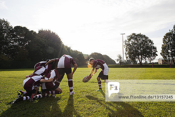 Teenage schoolboy rugby team taking ball from huddle