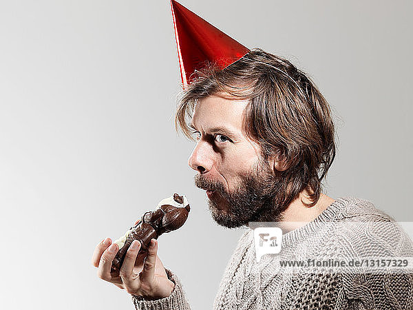 Mid erwachsenen Mann in Partei Hut essen Schokolade vor weißem Hintergrund