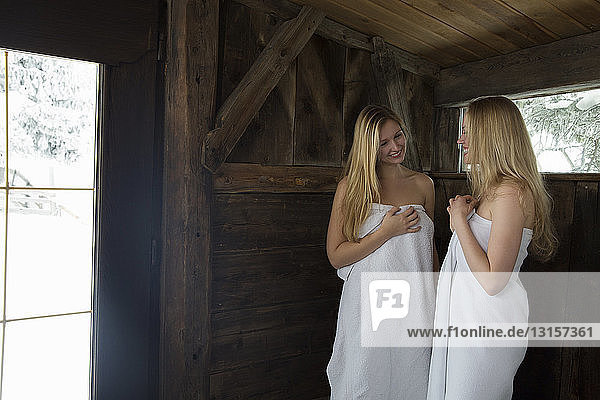 Zwei junge Frauen stehen in der Sauna  eingewickelt in ein weißes Handtuch