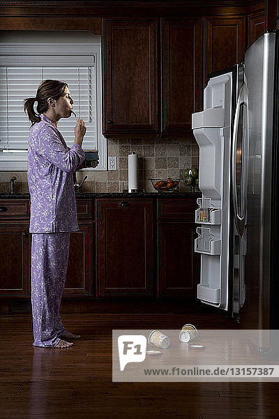 Woman in pyjamas  eating ice cream in front of refrigerator