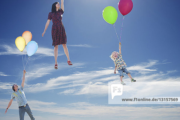 Älteres Paar und junger Sohn schweben in den Himmel und halten sich an Ballons fest
