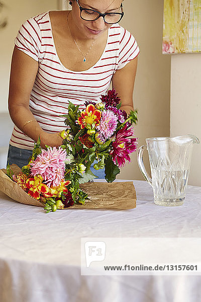 Mid adult woman unwrapping flowers in dining room