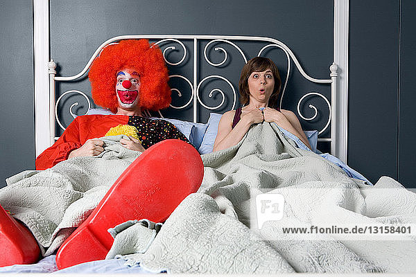 Clown and woman surprised to find themselves in bed together