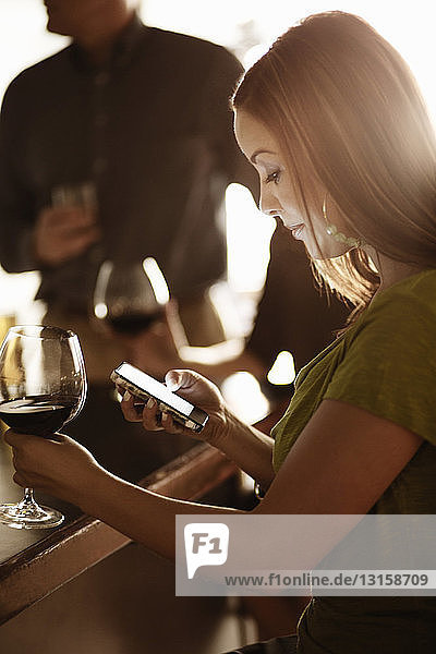 Geschäftsfrau schaut in einer Weinstube auf ihr Handy