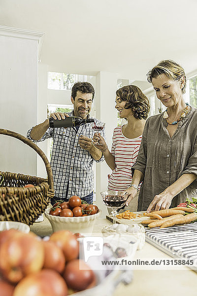 Drei Erwachsene schenken Rotwein ein  während sie frisches Gemüse zubereiten