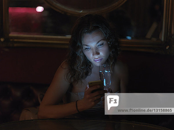 Mittlere erwachsene Frau sitzt nachts in einer Bar und benutzt ein Smartphone