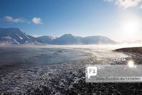 Blick auf die sonnenbeschienene Küste und die fernen Berge  Svalbard  Norwegen