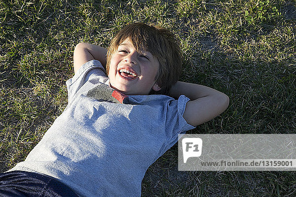 Porträt eines Jungen  der lachend auf dem Rasen eines Parks liegt