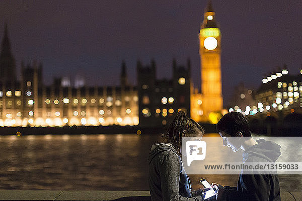 Seitenansicht junger Frauen mit Smartphones gegenüber dem Palace of Westminster  London  UK