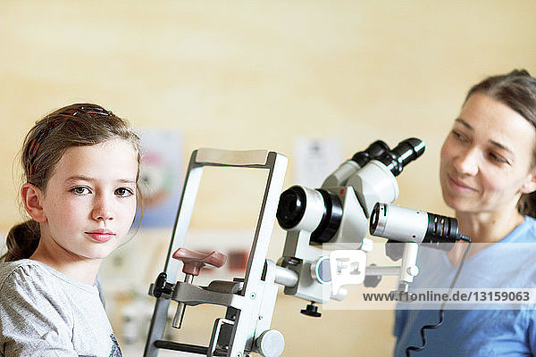 Optikerin bereitet sich auf die Untersuchung der Augen eines Mädchens vor