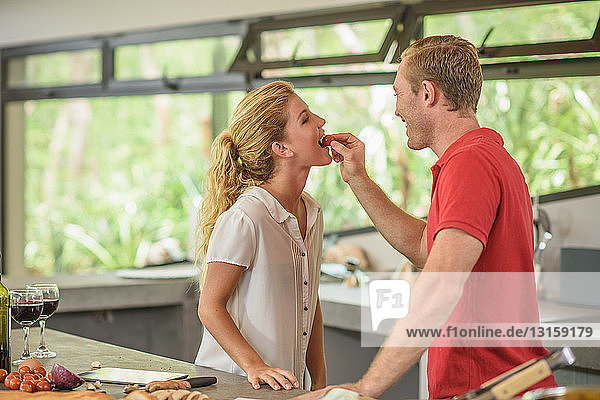 Mann füttert seine Freundin in der Küche mit Tomaten