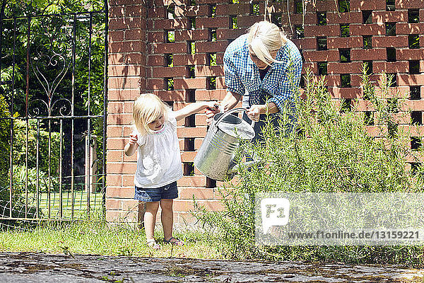 Weibliches Kleinkind hilft Mutter mit Gießkanne im Garten