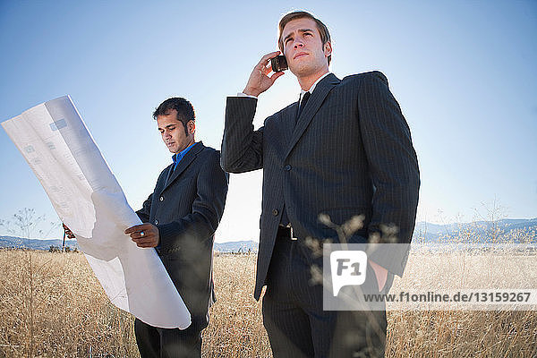 2 Männer mit Plänen im Feld  einer am Telefon