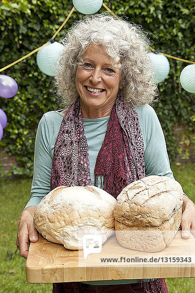 Porträt einer reifen Frau mit Brotlaiben bei einem Gartenfest