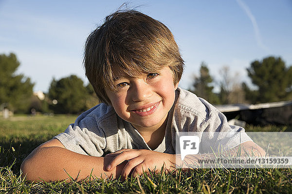 Porträt eines lächelnden Jungen  der auf dem Rasen eines Parks liegt
