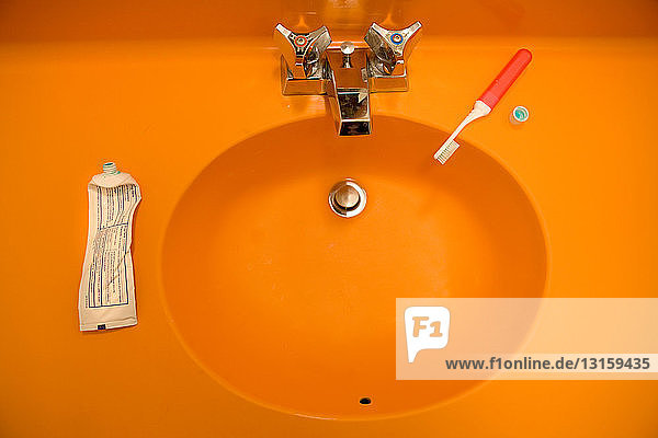 Orangefarbenes Waschbecken mit Zahnbürste und Zahnpasta