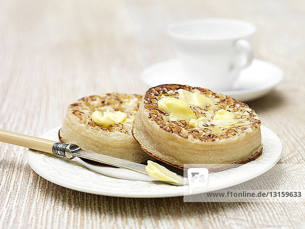Melting butter on toasted crumpets with butter knife on plate