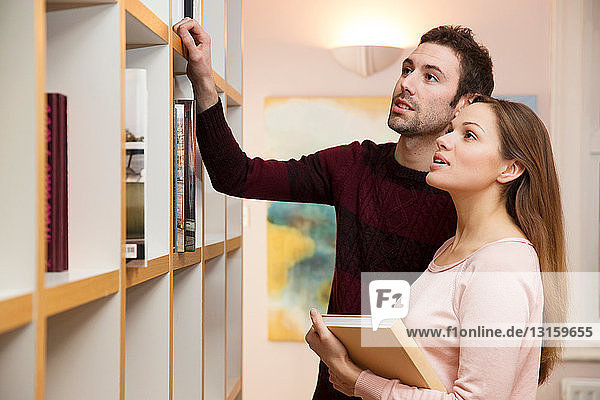 Junges Paar wählt ein Buch aus dem Bücherregal aus