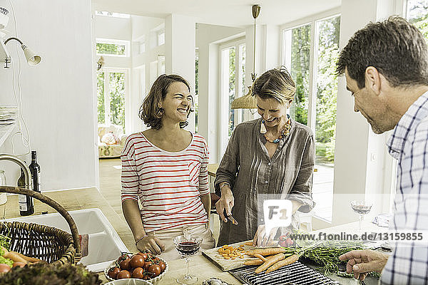 Drei Erwachsene unterhalten sich bei der Zubereitung von frischem Gemüse in der Küche