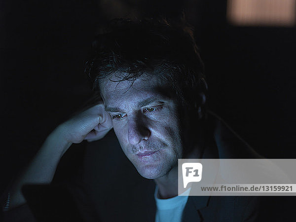 Mid adult man using digital tablet at night face illuminated