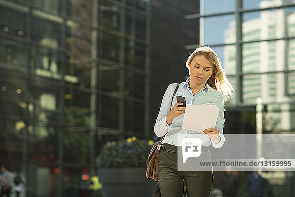 Young city businesswoman reading paperwork outside office
