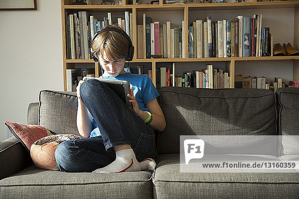 Junge  der über Kopfhörer Musik hört und ein digitales Tablet benutzt
