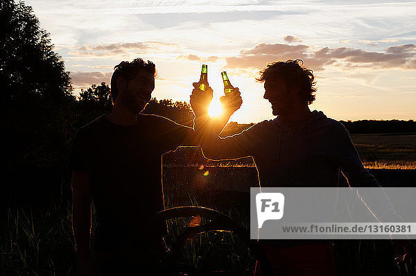 Silhouette von Männern  die bei Sonnenuntergang ein Bier trinken